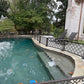Removable dog pool fence following the curved edge of a freeform pool along the pool steps, separating the water from the lounge chair area