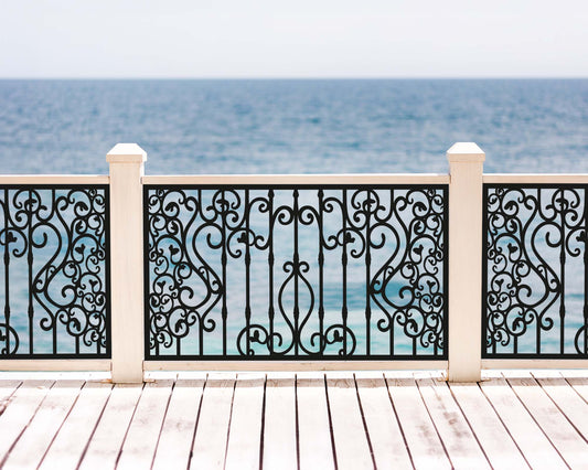 Black powder coated laser cut metal outdoor deck railing panel featuring traditional wrought iron scrollwork installed on seaside wooden patio
