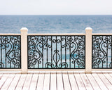 Black powder coated laser cut metal outdoor deck railing panel featuring traditional wrought iron scrollwork installed on seaside wooden patio