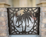 Black powder coated laser cut metal pedestrian garden gate featuring tropical palm tree beach motif installed between natural stone pillars