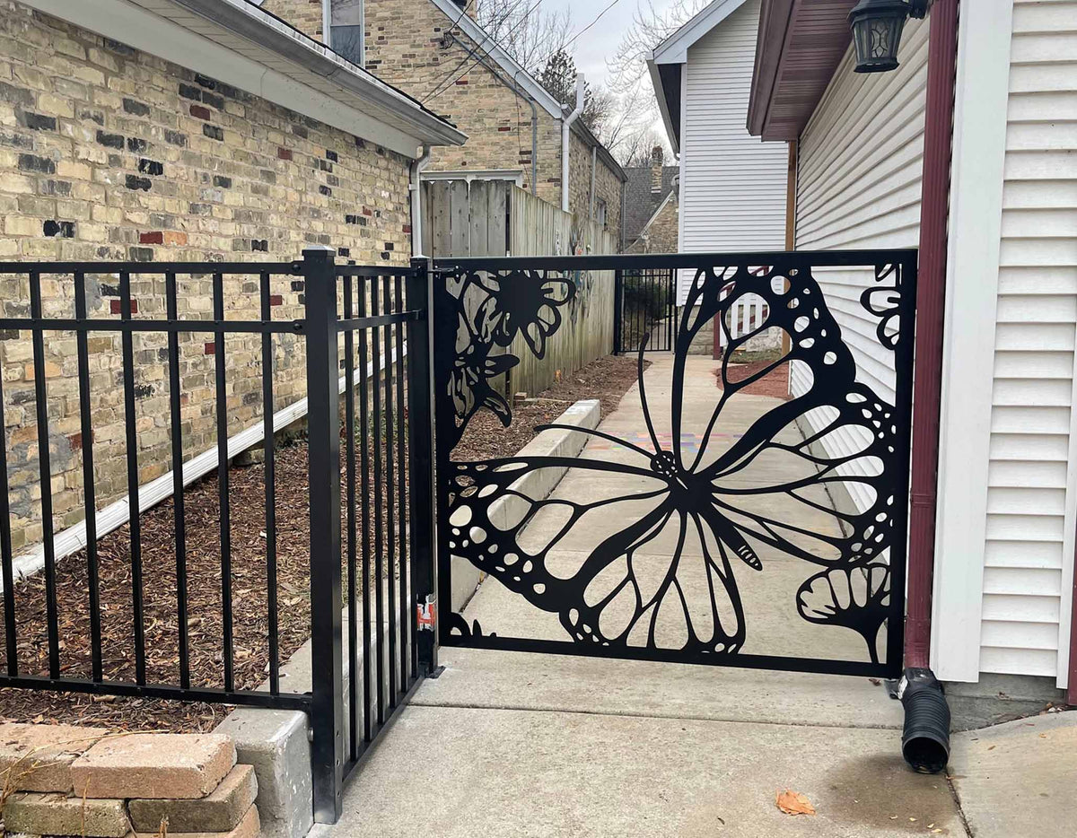 Black powder coated laser cut metal side pedestrian gate featuring large monarch butterfly wing and flower pattern installed next to residential fence