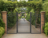 Black powder coated metal pedestrian garden gate with side panels featuring central heart motif and arched top frame installed between brick pillars