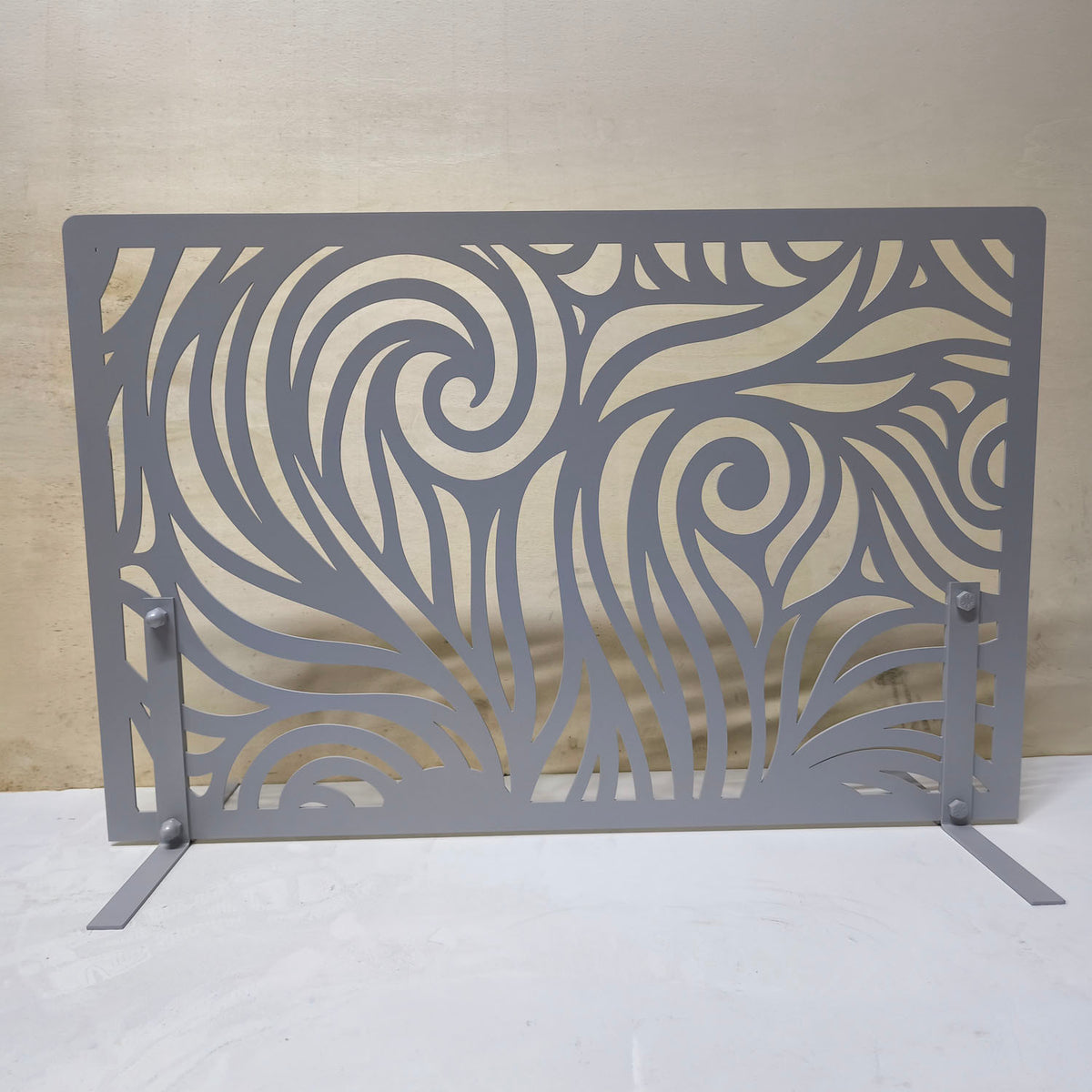 Freestanding grey metal fireplace screen with modern decorative laser cut wave pattern