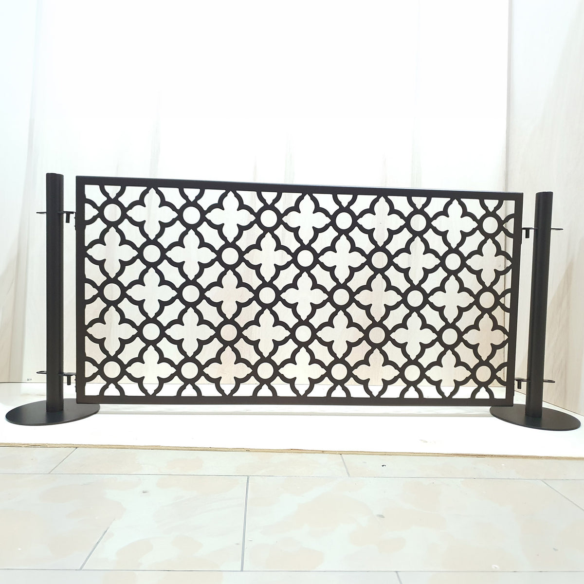 Front view of a black freestanding dog pool fence panel with quatrefoil laser cut pattern mounted between two round base stainless steel posts