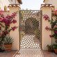 Laser cut metal garden gate with a cobblestone spiral vortex pattern in matte beige grey (RAL 7006), set in a Spanish-style courtyard with stucco pillars and pink bougainvillea.