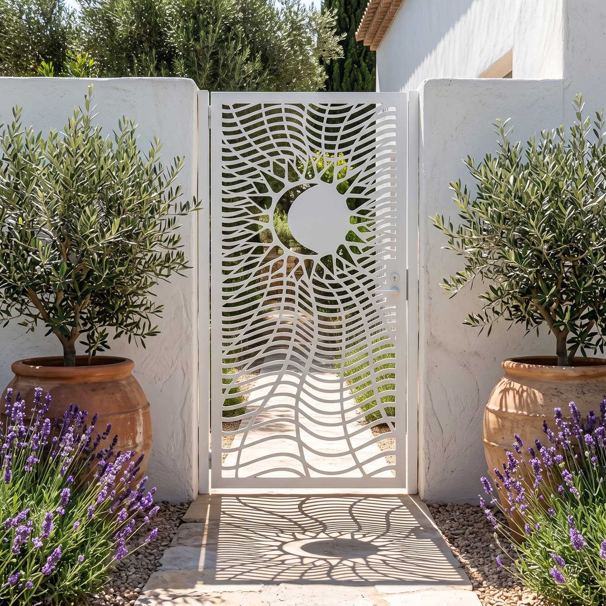 Laser cut metal garden gate with a sun and moon eclipse pattern, powder-coated in matte white, set between white stucco walls with potted olive trees and lavender.