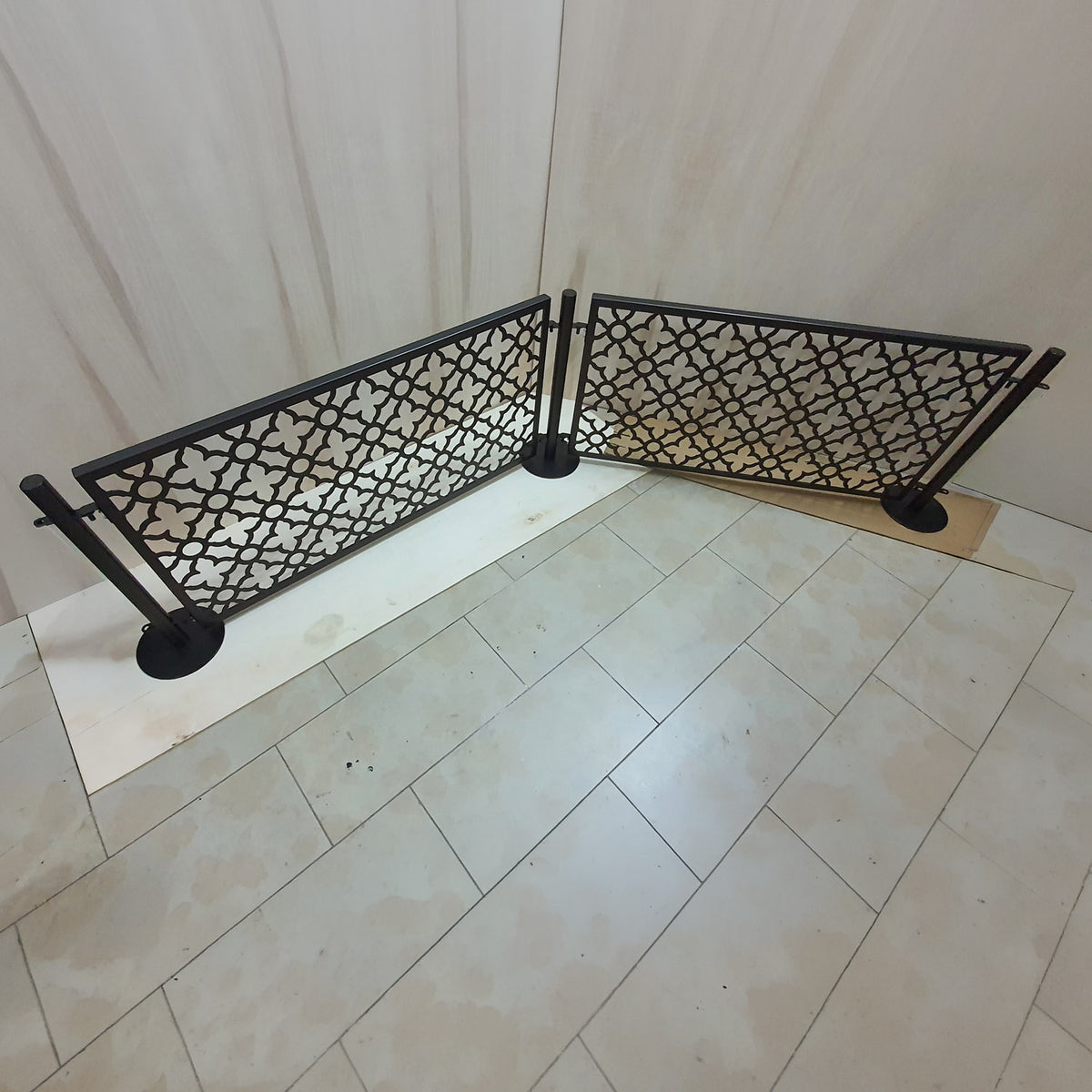 Modular freestanding dog pool fence set with two laser cut panels and three round base posts arranged at an angle on a tile floor