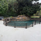 No drill freestanding dog pool fence installed on a concrete pool deck without anchors, panels angled around a rock waterfall pool