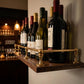 Unlacquered solid brass gallery rail shelf guard holding wine bottles on a dark wood home bar floating shelf.
