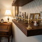 Close-up view of polished unlacquered solid brass gallery rail mounted on a dark wood shelf holding vintage collectibles and picture frames.