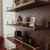 Solid unlacquered brass gallery rail guards mounted on dark walnut wood open floating shelves displaying decor items and books.